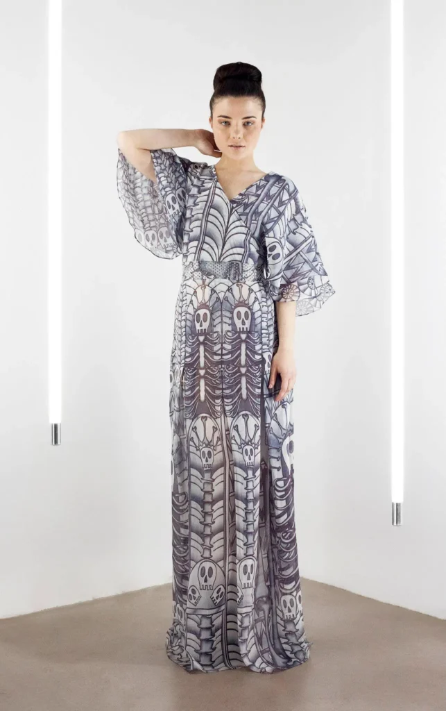 Model wearing a grey silk georgette wrap kaftan with kimono sleeves and a waistband printed with Pac-Man-style skull motifs.